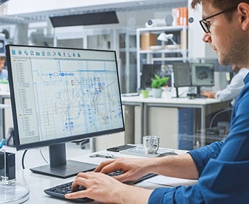 Over the Shoulder Shot of Engineer Working with CAD Software on Desktop Computer, Screen Shows Technical Drafts and Drawings. In the Background Engineering Facility Specialising on Industrial Design